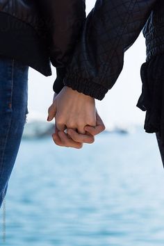 two people holding hands while standing next to each other in front of the ocean and sky