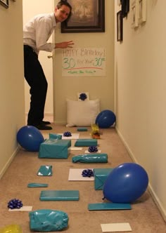 a man is standing in the hallway with balloons and gifts on the floor next to him