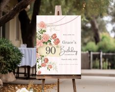 an easel with a sign that says 90th birthday on it and flowers in the foreground