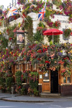 the outside of a pub covered in flowers and hanging from it's walls with flags