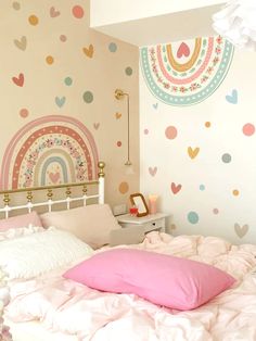 a white bed topped with pink pillows next to a wall covered in rainbows and hearts