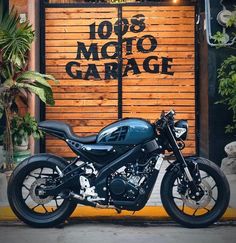 a black motorcycle parked in front of a garage door with the words 1018 moto garage written on it