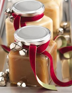 three jars filled with different types of candles and ribbons on top of a table next to silver bells