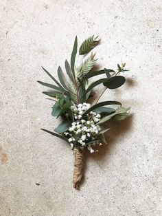 a boutonniere with white flowers and greenery on the floor in front of a wall