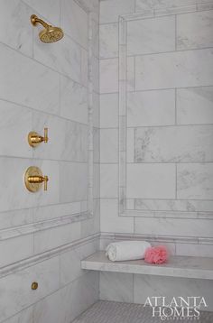 a white bathroom with gold fixtures and marble tiles on the shower wall, along with a pink tissue roll