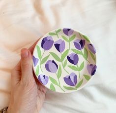 a hand holding a purple and green plate on top of a white bed with sheets