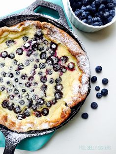 a blueberry pie with powdered sugar on top and berries around the edges, in a cast iron skillet