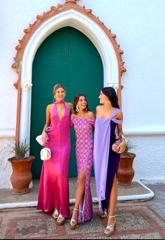 three beautiful women standing next to each other in front of a green door wearing dresses