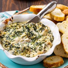 spinach dip in a white bowl on a blue plate with crackers and bread