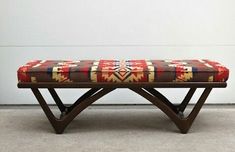 a wooden bench with a colorful blanket on it's backrest in front of a white wall