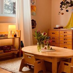 a wooden table sitting in front of a window next to a dresser with flowers on it