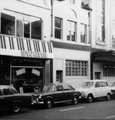 an old black and white photo of cars parked in front of a building