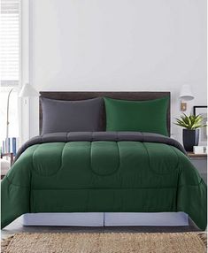 a bed with green and grey comforters in a room next to a window,