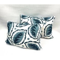 two blue and white pillows sitting on top of a bed next to eachother