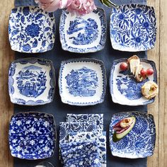 blue and white plates are arranged on a wooden table with pink flowers in the background