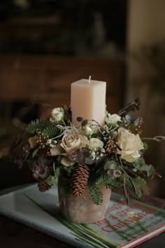 a candle is sitting on top of a table with flowers and pine cones in it