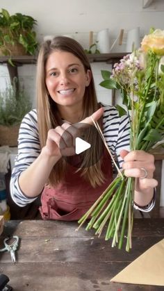 a woman holding flowers in her hands and pointing to the camera while making a flower arrangement