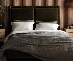 a bed with two pillows on top of it next to a night stand and lamp