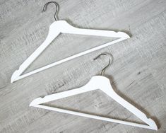 two white clothes hangers sitting on top of a wooden floor next to each other