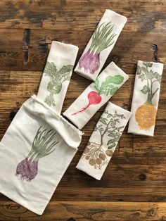 four napkins with vegetables printed on them sitting on a wooden table next to each other