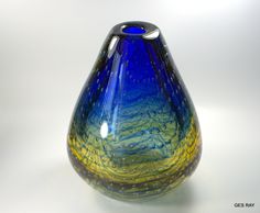 a blue and yellow glass vase sitting on top of a white tableclothed surface