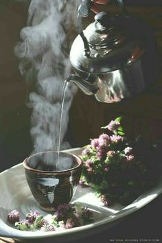 steam rising from a teapot into a bowl on a plate with flowers in the foreground