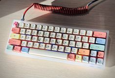 a computer keyboard sitting on top of a wooden desk next to a power cord and mouse