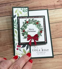 a hand holding up a christmas card on top of a wooden table next to a red ribbon