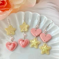 "These clay heart and star dangle earrings are handmade from polymer clay and add a kawaii touch to any outfit. The stars even glow in the dark! Made from special iridescent clay that shimmers in the light and embellished with an iridescent pink bead. - Dimensions: 1.5\" tall (2.5\" with earring hooks) - Silver-plated surgical steel hypo-allergenic earring hooks - Heart and star is coated in UV resin for protection and shine Available in two designs - heart or star dangle." Polymer Clay Star Earrings, Cute Earrings With Dangling Charms For Gifts, Cute Heart Charm Earrings For Party, Cute Party Earrings With Heart Charm, Playful Heart-shaped Earrings For Parties, Playful Heart-shaped Party Earrings, Playful Heart Shaped Party Earrings, Cute Star Charm Dangle Earrings, Cute Dangle Earrings With Star Charm