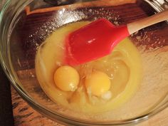 two eggs in a glass bowl with a red spatula on the side and other ingredients