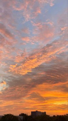 an airplane is flying in the sky at sunset with clouds and buildings behind it as the sun sets