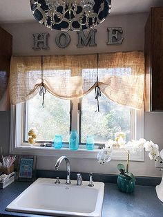 a kitchen sink under a chandelier in front of a window with the word mom on it