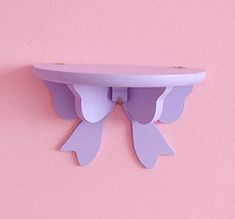 a pink wall with a purple shelf on it's side and two white wings hanging from the top