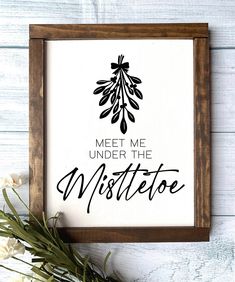 a framed sign with the words meet me under the mistcote on it next to some flowers