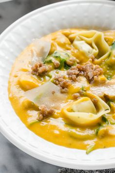 a white bowl filled with pasta and meat in sauce on top of a marble table