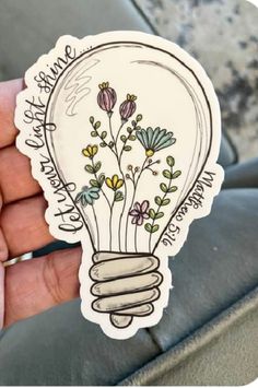 someone is holding up a sticker with flowers inside of the light bulb on it