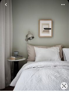 a bed with white sheets and pillows in a bedroom next to a painting on the wall