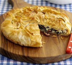 a wooden cutting board with a pie on it and a bowl of salad in the background