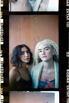 two women standing next to each other in front of a wooden wall and one woman with curly hair