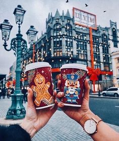 two people holding up coffee cups in front of a city street with lights and buildings