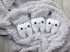 three tooth shaped key chains on top of a white blanket with eyes and teeth drawn on them