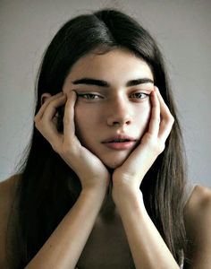 a woman with long hair holding her hands to her face and looking at the camera