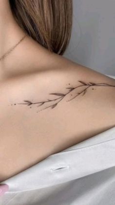 the back of a woman's shoulder with a small branch tattoo on her left side