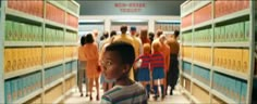 a young boy standing in front of a row of lockers filled with yellow and orange boxes