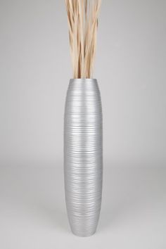 a tall silver vase with grass sticking out of it's sides on a grey background