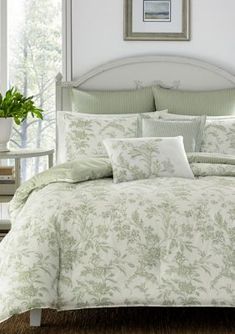 a bed with green and white comforters in a bedroom next to a painting on the wall