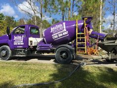 a purple tanker truck parked on the side of a road next to a yellow ladder