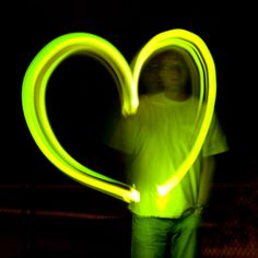 a man holding a neon heart in the dark