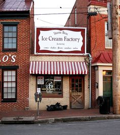 an ice cream factory on the corner of a street in front of brick buildings with red and white awnings