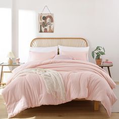 a bed with pink comforter and pillows in a white room next to a table